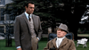 A man in a suit stands with his hand in his pocket, watching an older man seated outside a grand building—an evocative suspense thriller scene reminiscent of Sean Connery’s "Woman of Straw (1964) DVD.
