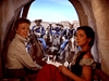 Two women sit inside a covered wagon, looking back toward soldiers and a stagecoach under a bright blue sky—a striking scene from vintage classic movies like Fort Yuma (1955) DVD.