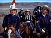 A group of men in old-fashioned military uniforms ride horses across a dry landscape, one holding a flag—all in wide-brimmed hats—in "Fort Yuma (1955) DVD," evoking classic Western movies.