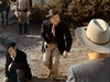 A man in a cowboy hat and scarf aims a gun outdoors, while another man sits nearby and two more are partially seen—just one intense moment from Five Guns West (1955) DVD, a rare vintage classic movie.
