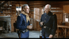 Two men in blue military uniforms stand in a rustic wooden room, holding drinks and chatting—a scene reminiscent of moments depicted in the 7th Calvary (1956) DVD before the Battle of Little Bighorn.