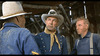Three men in old Western attire converse inside a wooden building; one, evoking a Battle of Little Bighorn officer with a decorated hat and yellow scarf, recalls scenes from the 7th Cavalry (1956) DVD.