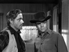 Two men in western attire—one in a vest, graying hair; the other in a cowboy hat and button-up—stand indoors by wood walls and curtains, evoking classic scenes from films like Five Guns to Tombstone (1960) DVD.
