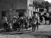 A group in cowboy hats and western attire rushes from a building labeled Tombstone Bank on a dusty street, evoking the spirit of vintage classics like Five Guns to Tombstone (1960) DVD in this quaint, old-fashioned town with a horse nearby.