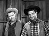 Two men in cowboy hats and western attire stand indoors by wooden walls, both looking at the camera with relaxed expressions. The black-and-white photo evokes the vintage charm of classics like Five Guns to Tombstone (1960) DVD.