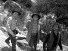 Three men in cowboy attire stand on rocky terrain, looking upward with concern—a scene evocative of classic Westerns. Capture the vintage wilderness with the Five Guns to Tombstone (1960) DVD.