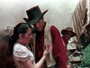 A woman looks at her hand in concern as a cowboy supports her, with another man and a horse by a covered wagon—evoking a classic scene from "The Cimarron Kid (1952)" DVD.