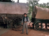 A man in cowboy attire stands between two covered wagons, evoking a classic Western—an ideal scene for fans of vintage films like The Cimarron Kid (1952) on DVD.
