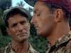 Two men in military uniforms stand outdoors, one gazing at the other with eyes closed; both wear caps and camouflage shirts amid greenery—a striking scene from the vintage classic World War II film Ambush Bay (1966) on DVD.