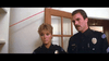 Two police officers—a blonde woman and a mustachioed man—stand seriously indoors before a glass-paneled wooden door, capturing the intense vibe of a scene straight from the Runaway (1984) DVD.