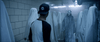 Wearing a baseball cap, someone faces a hallway of ghostly figures in a dim, eerie scene from Haunt (2019) DVD. One sinister figure in a mask and striped robe stands out, evoking the feel of an extreme haunted house.