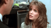 A woman in a checkered blazer looks up at a man with concern, echoing a tense scene from In the Arms of a Killer (1992) DVD; blurred office items fill the indoor background.