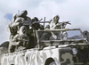 A group of armed figures in camo gear ride in an open-top vehicle, rifles at the ready—reminiscent of a scene from Warhead (1977) DVD—set against a cloudy sky.