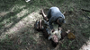 In a forest clearing, a person kneels over another, offering aid as sunlight filters through the trees—a scene reminiscent of classic moments from the Citizen X (1995) DVD.