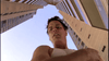 A man in a white tank top looks down intensely from between tall buildings beneath a clear sky—a scene evoking the suspense of "Murder Most Likely (1999) DVD.