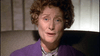 A woman with short curly hair in a purple sweater sits in a chair, looking concerned at the camera—reminiscent of a scene from "Murder Most Likely (1999)" on DVD—softly lit against a neutral background.
