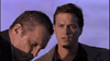Two men stand outdoors; one in front looks down seriously, the other gazes ahead thoughtfully. The bluish-purple tint adds a cinematic vibe—ideal for fans of classic films like Murder Most Likely (1999) on DVD.