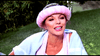 A woman outdoors smiles with greenery behind her, wearing a light pink knit headband and white tank top—her style reminiscent of Joan Collins in The Cartier Affair (1984) DVD.