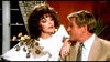 A woman in a white sequined dress leans on a man in a beige suit, echoing the glamour of Joan Collins films and rare finds like The Cartier Affair (1984) DVD.
