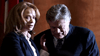 A woman in a business suit stands beside an older, distressed man, offering comfort—a scene reminiscent of a tense moment from the true crime drama "Too Late To Say Goodbye (2009) DVD.