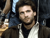 A serious man with tousled brown hair and a scruffy beard, dressed in a light shirt and brown jacket, stands ahead of others in casual wear—evoking the hero from the "Snake Eater (1989) DVD.