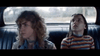 Two young people sit in a car’s backseat—the left with curly hair and a serious look, the right in stripes glancing upward—echoing the suspenseful mood of classic thrillers like The Black Phone (2021) DVD.