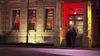 Two people approach a columned building with a red neon sign reading The Claremont, illuminated at night—reminiscent of scenes in Mrs. Palfrey at the Claremont (2005) DVD, ideal for collectors of rare movies on DVD.