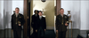 Two men in military uniforms stand at attention by an open doorway as two men in dark suits walk through, echoing the style of a classic WWII film; a white bust and decorative vase appear in the background. Product: Emperor (2012) DVD.