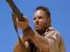 A rugged man with short hair and a tan shirt aims a rifle upward under a clear sky, evoking scenes from vintage adventure films like the Sahara (1995) DVD.