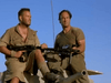 Two men in military gear sit on a tank under clear blue skies, each holding a machine gun—capturing the vintage action vibe of Sahara (1995), now available on DVD.