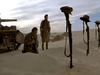 Two soldiers in desert uniforms honor graves marked with helmets atop rifles in the sand; a tank appears on the left beneath a partly cloudy sky—recalling scenes from the classic film "Sahara (1995)" DVD.