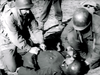 Two soldiers in uniform kneel beside a third on the ground, aiding him in a dramatic black-and-white wartime scene—capturing the intensity of vintage films like Then There Were Three (1961) DVD.