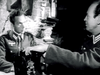 Two men in WWII-era uniforms sit indoors—a serious one facing forward, the other gesturing across the table. This tense, dimly lit scene captures vintage drama like "Then There Were Three" (1961) on DVD.