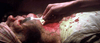 A close-up of a person with wounds and blood, as a hand uses a fork on their neck—an intense, graphic moment reminiscent of the shocking scenes found in "Feast (2005)" on DVD.