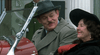 A man in a trench coat and hat sits smiling beside a woman in classic attire in a red vintage car, evoking the style of the true crime film "A Is For Acid (2002) DVD.