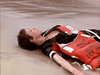 A person in a black shirt and red life jacket lies exhausted on wet sand, reminiscent of a scene from the "Trouble in Paradise (1989) DVD.