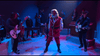 A man dressed as Santa sings on stage with a rock band and brass musicians, illuminated by colorful lights—capturing the festive spirit of The Christmas Chronicles (2018) DVD.