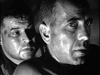 Two men with intense, serious expressions—one in front, one behind—are shown in close-up, faces sweaty and partly lit. This powerful image captures the tension of Free French forces in Passage to Marseille (1944) DVD.