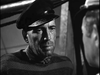 A man in a sailor’s cap, striped sweater, and scarf stands under dramatic lighting in a black-and-white scene from Passage to Marseille (1944) DVD, reminiscent of Humphrey Bogart’s iconic role, facing another partially visible person.