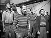 A group of sailors in striped shirts and high-waisted pants stand on deck, looking upward with serious expressions—reminiscent of the Free French forces in the black-and-white film Passage to Marseille (1944), now available on DVD.