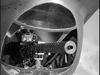 A person in goggles and a flight helmet aims a machine gun from a military aircraft turret, evoking scenes from Passage to Marseille (1944) DVD starring Humphrey Bogart, looking through the gun sight.