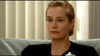 A blonde woman with her hair pulled back, in a black top and small hoop earrings, sits calmly on a light couch by vertical blinds—resembling a scene from the "Chances Are (1989) DVD" starring Robert Downey Jr.