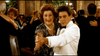 A young man in a white tuxedo dances with an older woman in a sparkly dress at a formal event, echoing scenes from the Chances Are (1989) DVD, as other couples waltz nearby to the orchestra’s music.