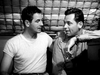 Two men, one in a white t-shirt and the other in a button-up shirt, sit close together and talk, with one’s arm around the other's shoulder—echoing scenes from classic films like Submarine Command (1951) DVD.