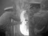 Two sailors in uniform urgently close a submarine hatch as smoke billows out—evoking scenes from vintage classics like the rare Submarine Command (1951) DVD.