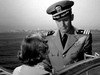 A man in a naval uniform stands on a boat, gazing at a woman with short hair. This black and white image from "Submarine Command (1951) DVD" evokes the timeless atmosphere of classic vintage films, with water and shoreline in view.