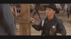 A sheriff in black stands by a wooden post in a Spaghetti Western scene, echoing Three Graves for a Winchester. Blurred people and horses form the background. Product: Three Graves for a Winchester (1966) DVD.