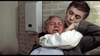 A tense scene unfolds like the Dead of Night (1974) DVD cover: in a restroom with a tiled wall and paper towel dispenser, a suited person is choked from behind by another with short hair, both appearing distressed.