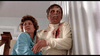 A woman in blue helps a distressed man in a bloodied white shirt as they stand by a curtain—an intense moment from the rare classic movie showcased on the Dead of Night (1974) DVD.
