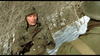 A man in a green winter military uniform raises his hands in surrender or caution amid the snowy Ardennes forest, facing another soldier. Leafless bushes set the tense WWII scene from "A Midnight Clear (1992)" DVD.